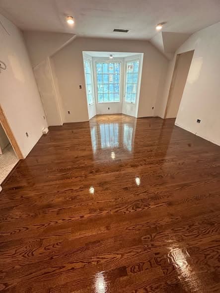 Highly polished dark wood floors reflecting light in an empty room with a bay window.