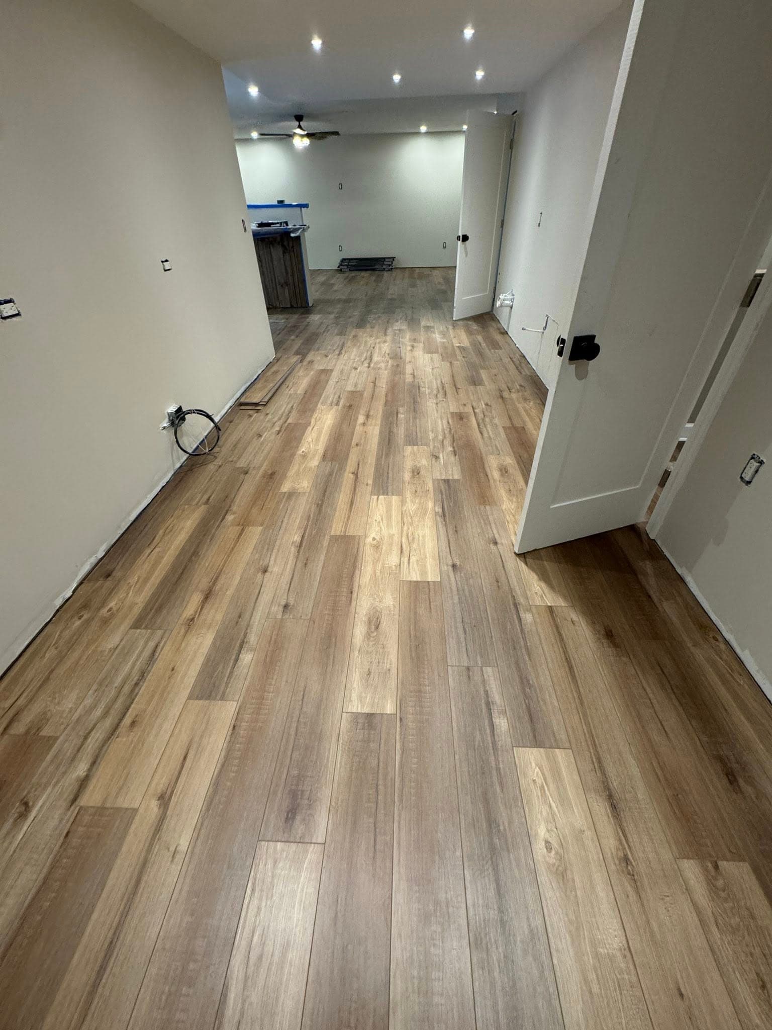 Newly installed light brown wood-look flooring in a renovated room with white walls and recessed lights.