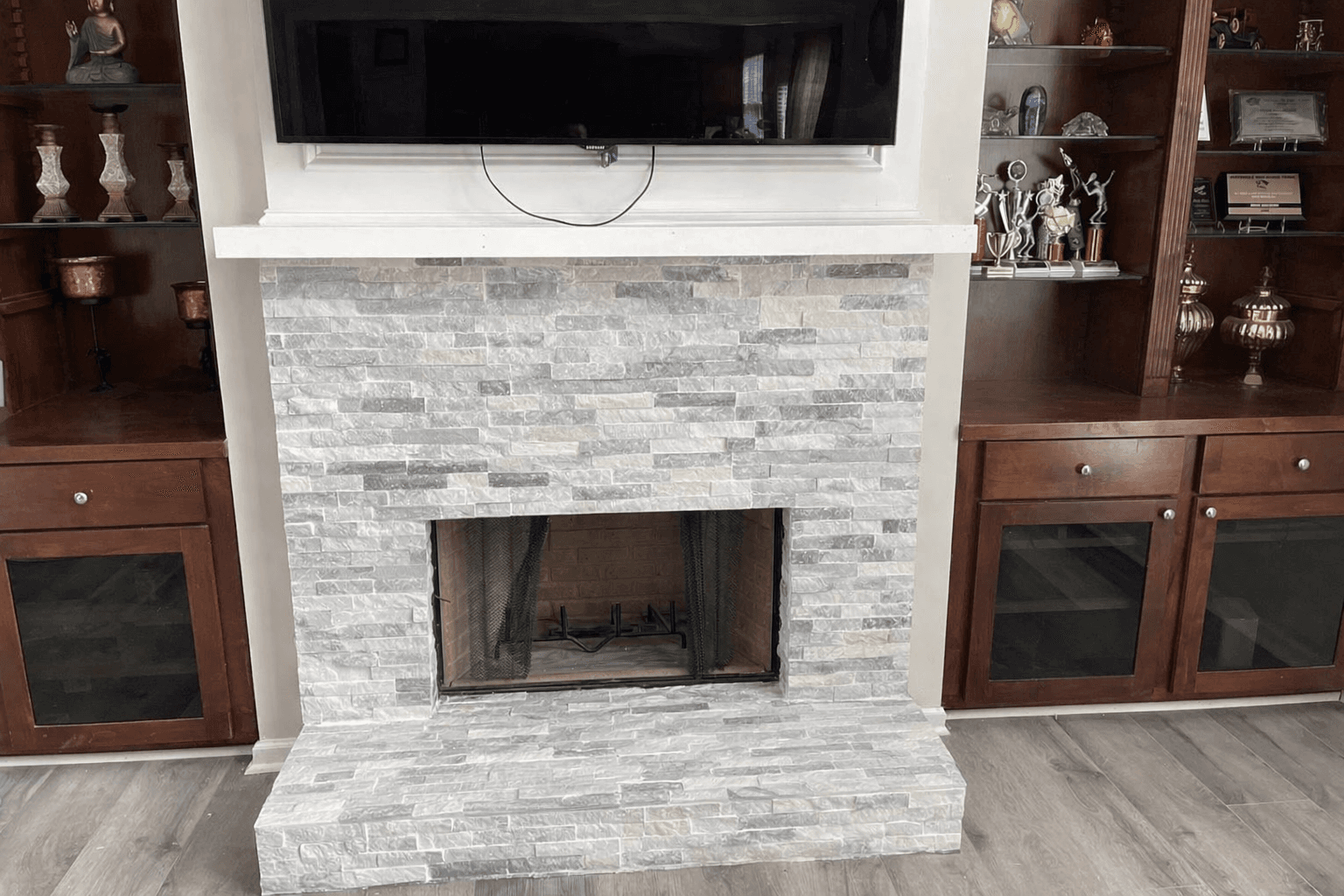 A grey stacked stone fireplace with a white mantel between dark wood built-in cabinets.